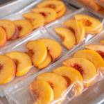 Frozen peach slices arranged in freezer bags on a tray, ready for smoothies, cobbler, and other peach recipes.