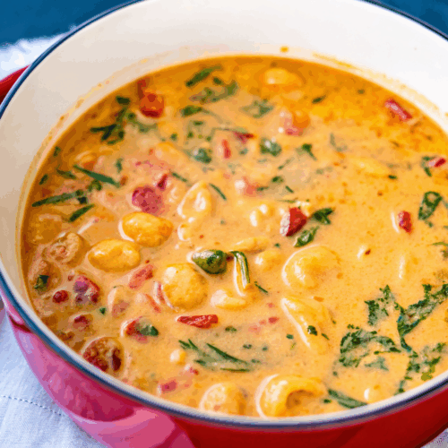 Red Dutch oven filled with creamy Marry Me Tuscan Chicken Soup with pasta, spinach, and sundried tomatoes.
