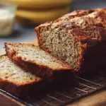 Slice of moist banana bread topped with nuts and a banana