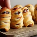 Mummy pigs in a blanket served on a festive platter for Halloween.